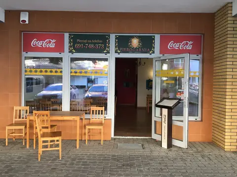 Lokal na parterze, przeszklone wejście z dwoma czerwonymi markizami; latem stoliki przed wejściem.
